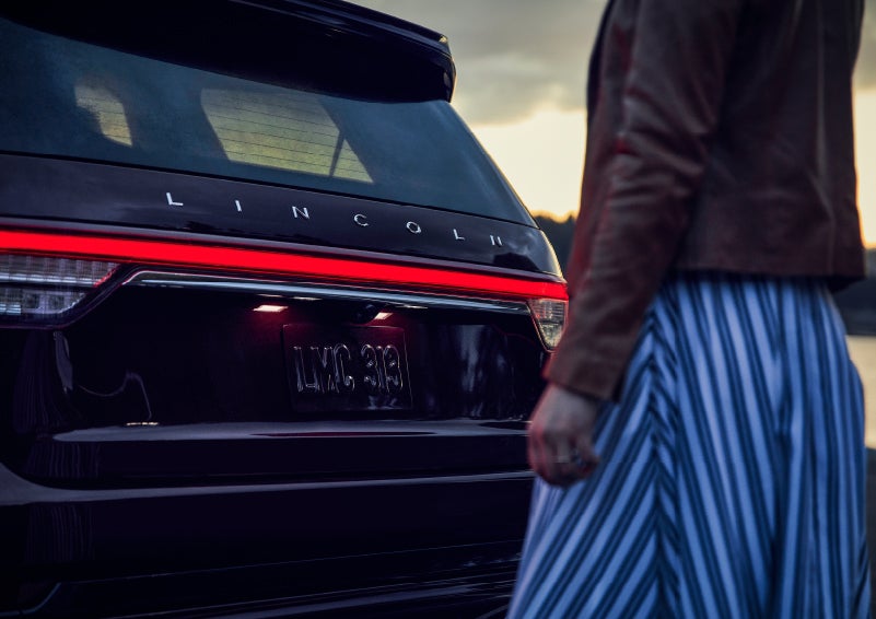 A person is shown near the rear of a 2024 Lincoln Aviator® SUV as the Lincoln Embrace illuminates the rear lights | McLarty Daniel Lincoln in Bentonville AR