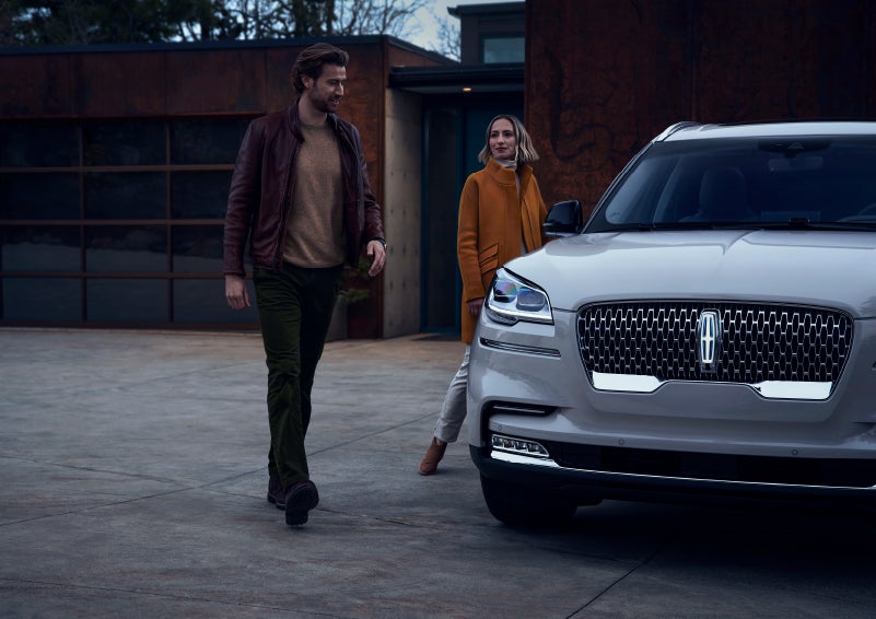 A man and a woman approaching a 2024 Lincoln Aviator® SUV, which illuminates certain lights when they are close | McLarty Daniel Lincoln in Bentonville AR