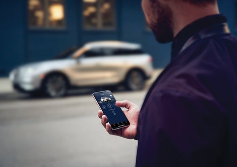 A person is shown interacting with a smartphone to connect to a Lincoln vehicle across the street. | McLarty Daniel Lincoln in Bentonville AR