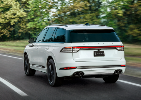 A white 2025 Lincoln Aviator® SUV is being driven away down a road lined with colorful trees. | McLarty Daniel Lincoln in Bentonville AR