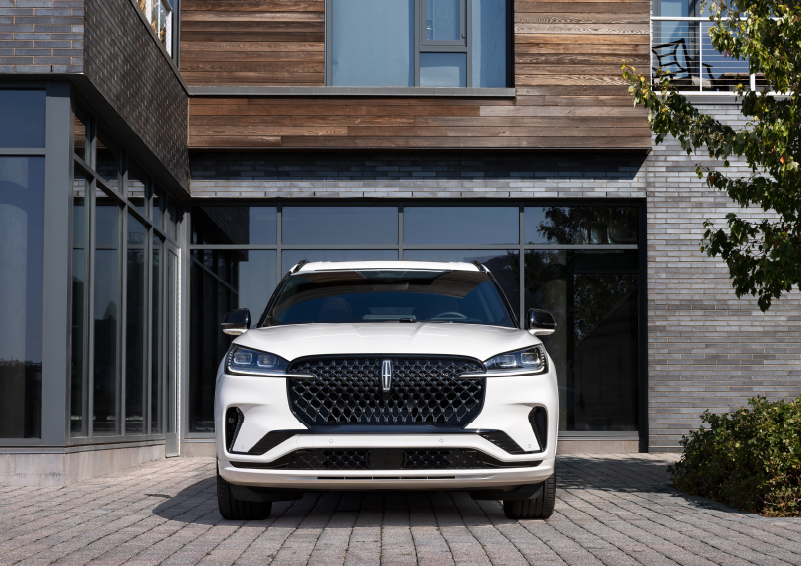 A white 2025 Lincoln Aviator® SUV is shown parked outside a modern building with gray brick and wood accents. | McLarty Daniel Lincoln in Bentonville AR