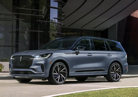 A gray 2025 Lincoln Aviator® SUV is parked outside a modern building showcasing the driver’s side of the vehicle. | McLarty Daniel Lincoln in Bentonville AR