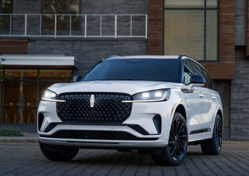 A white 2025 Lincoln Aviator® SUV is shown parked outside a modern building with gray brick and wood accents. | McLarty Daniel Lincoln in Bentonville AR