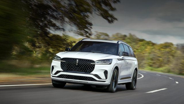 A white 2025 Lincoln Aviator® SUV is being driven down a road lined with trees. | McLarty Daniel Lincoln in Bentonville AR