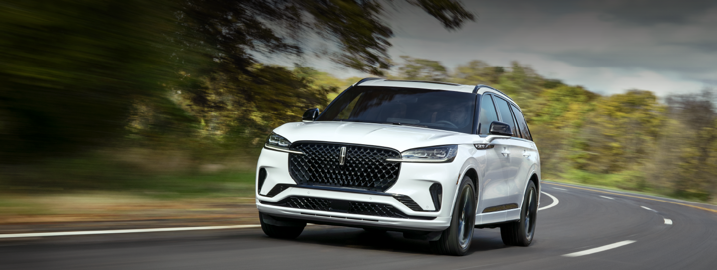 A white 2025 Lincoln Aviator® SUV is being driven down a road lined with trees. | McLarty Daniel Lincoln in Bentonville AR