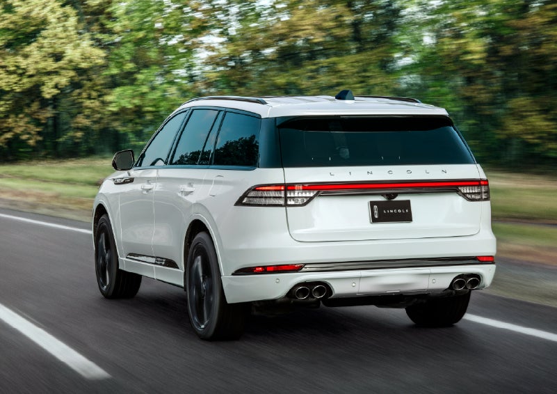 A white 2026 Lincoln Aviator® SUV is being driven away down a road lined with colorful trees. | McLarty Daniel Lincoln in Bentonville AR