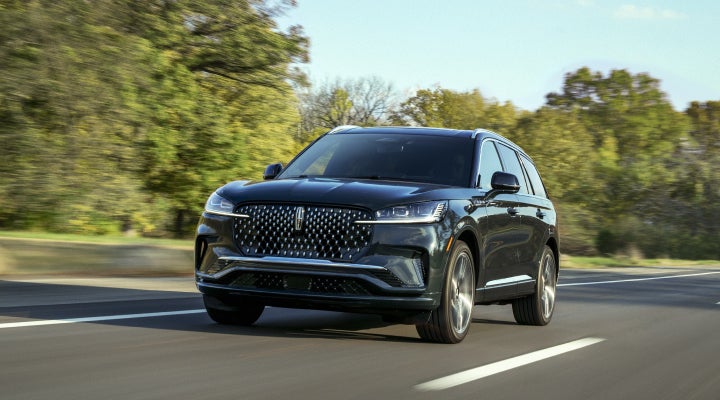 A 2026 Lincoln Black Label™ Aviator® SUV is being driven down a road lined with trees. | McLarty Daniel Lincoln in Bentonville AR