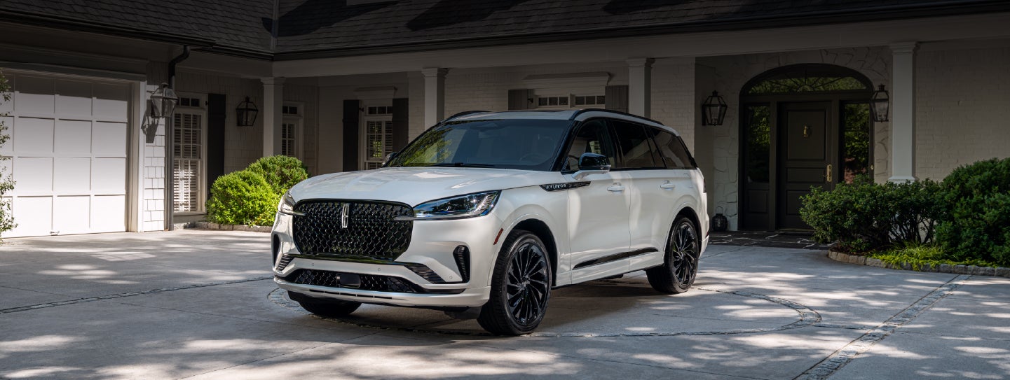A white 2026 Lincoln Aviator® SUV is parked in the driveway of a luxury home. | McLarty Daniel Lincoln in Bentonville AR
