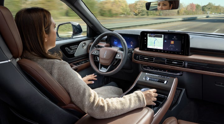 A 2027 Lincoln Aviator® SUV is being driven hands-free on a highway lined with trees. | McLarty Daniel Lincoln in Bentonville AR