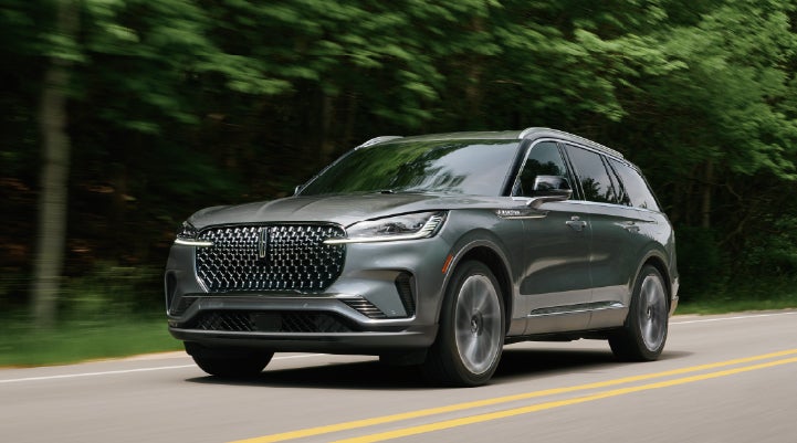 A 2027 Lincoln Aviator® SUV is being driven down a road lined with trees. | McLarty Daniel Lincoln in Bentonville AR